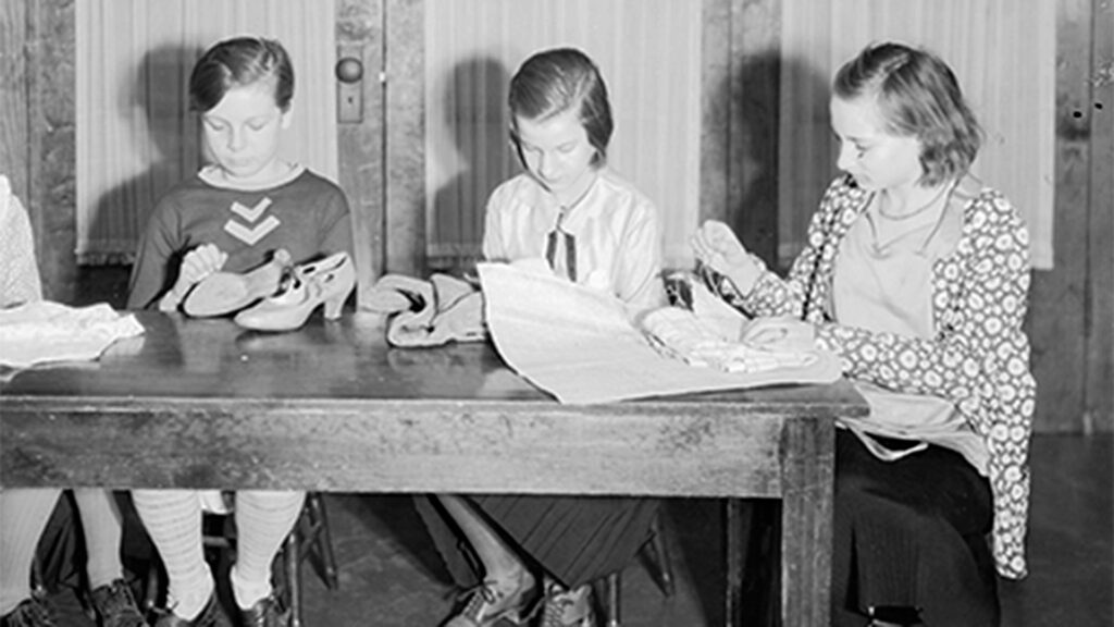 A historic image of three women sitting down while sewing fabric 