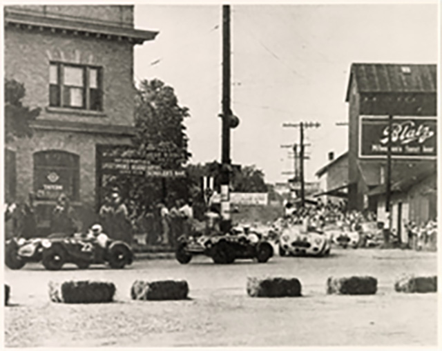 Sports cars race through downtown Elkhart Lake in 1952, with a mere snow fence and straw bales as protection for onlookers.