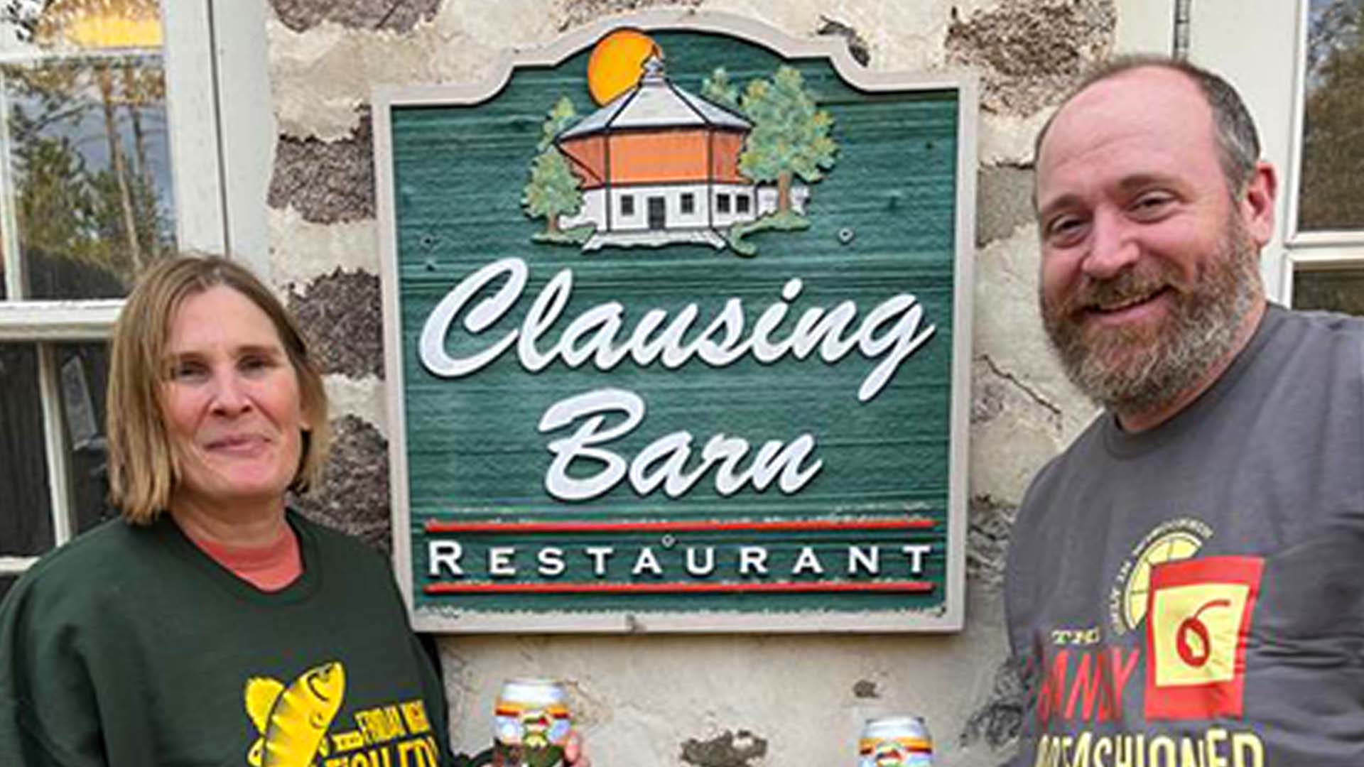 A man and woman standing by the Clausing barn Restaurant sign 
