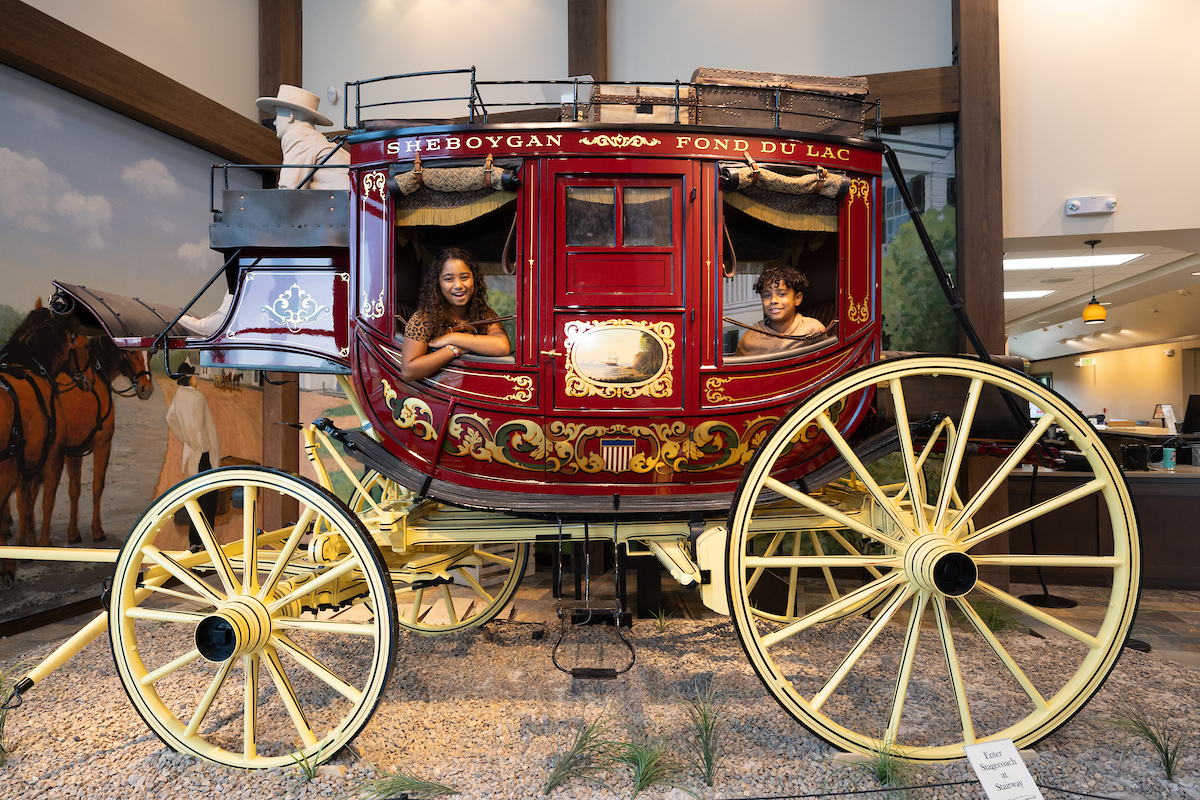 Two children pose in a stationary stage coach in the Carriage Museum.