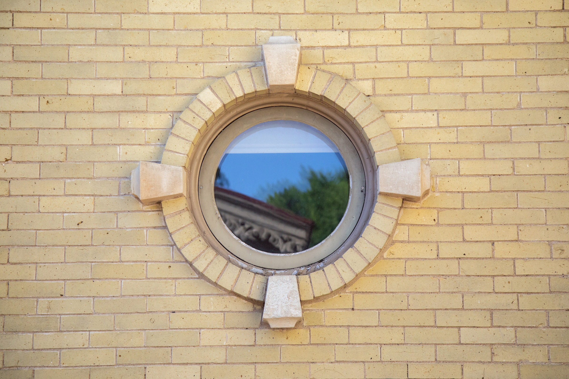 Circular window set within a light yellow brick wall.