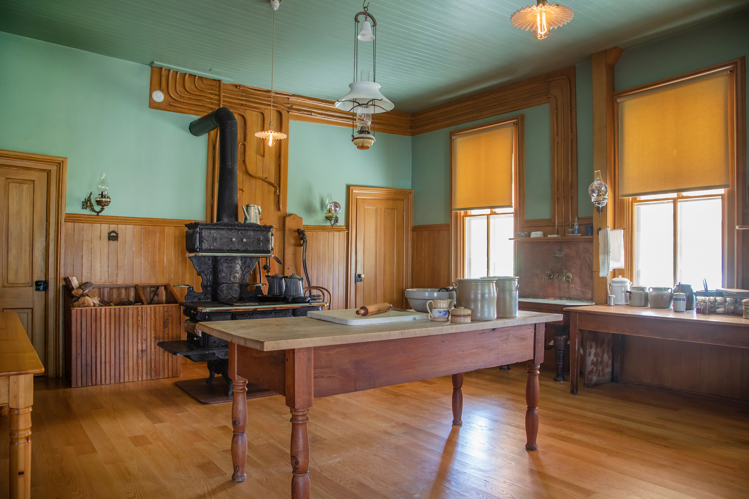 Antique kitchen with a wood stove, wooden cabinets, and a large wooden island countertop, with light green walls