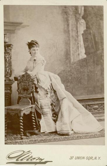 Full-length portrait of Nina Sturgis Dousman, wife of H. Louis Dousman, standing behind a chair.